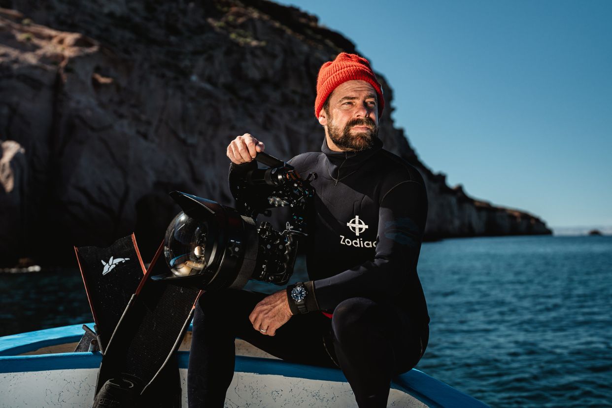 Andy Mann sits on the edge of a boat in diving gear with his camera.